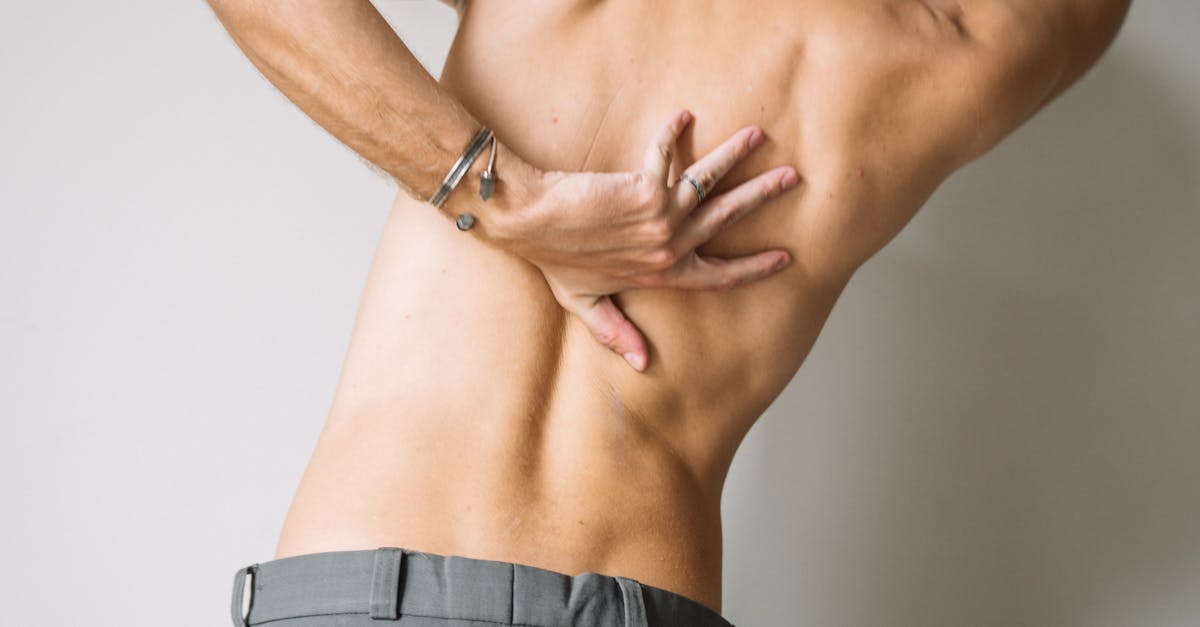 A shirtless man stretching his back indoors, showcasing muscular anatomy.